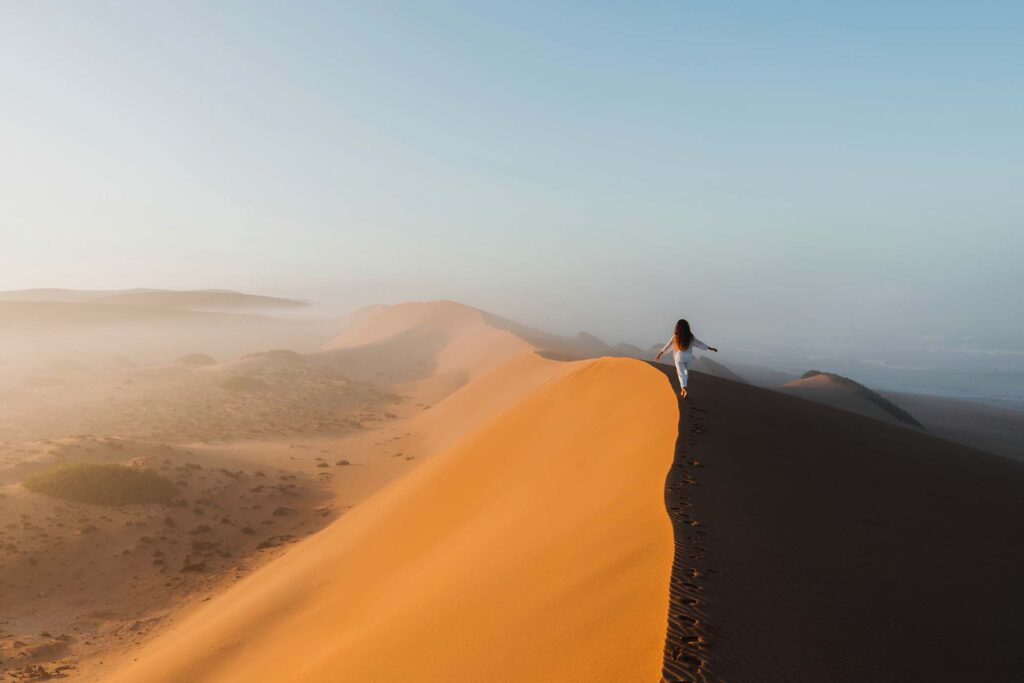 woman-walking-on-top-of-huge-sand-dune-in-morocco-6BVH67B.jpg